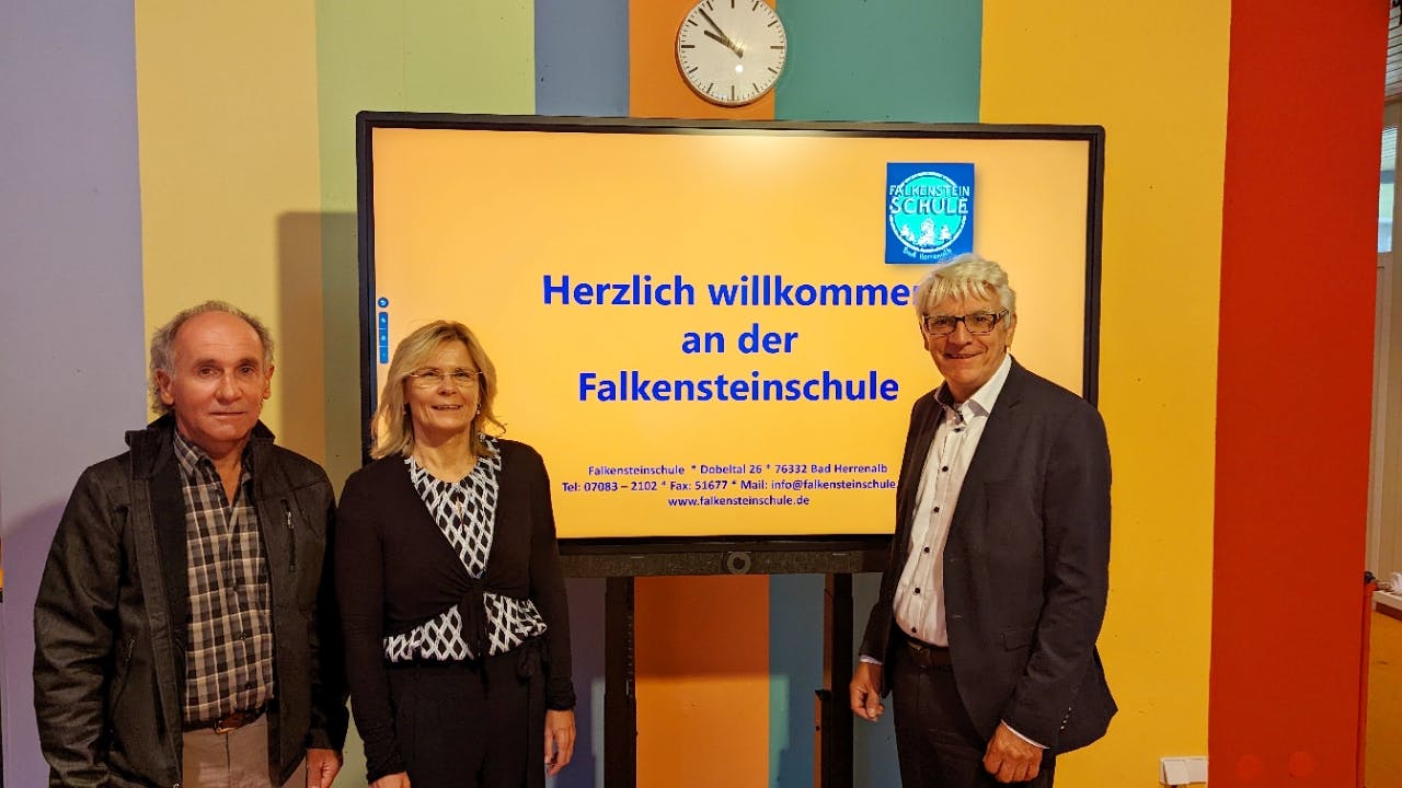 (v.l.:) Andreas Göhring, IT-Verantwortlicher der Stadtverwaltung, Rektorin Patricia Fischer und Bürgermeister Klaus Hoffmann vor dem Monitor in der Aula der Falkensteinschule. Auf dem Bildschirm werden die Schüler begrüßt und mit Infos versorgt.